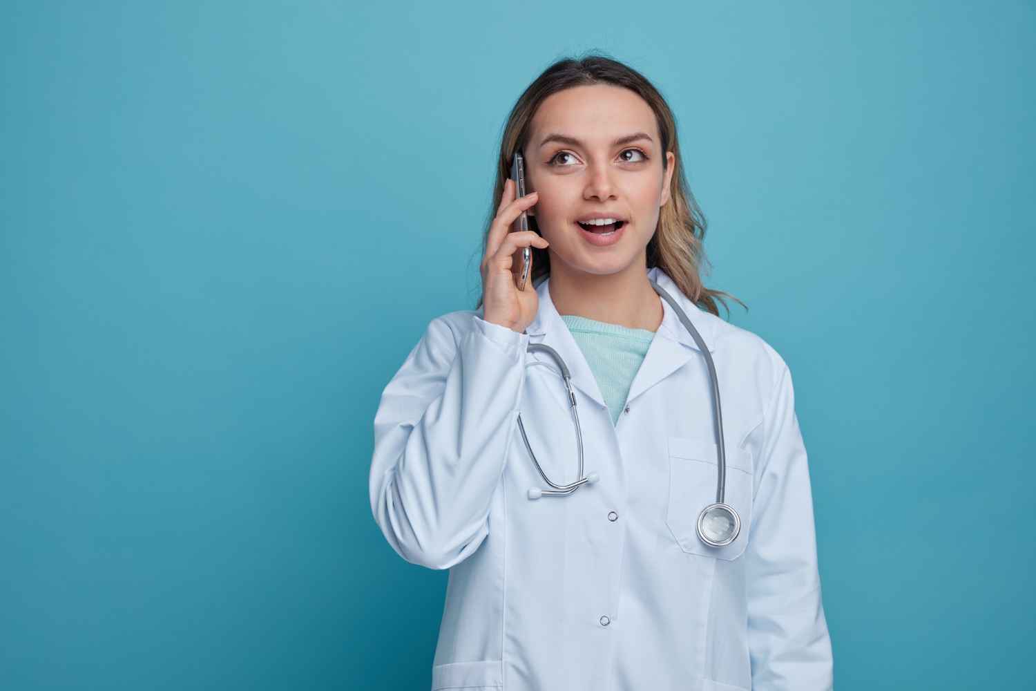 A female out-of-hours dentist in a white coat stands in a clinic hallway, taking an urgent call from a patient needing emergency dental care for a severe toothache or broken tooth